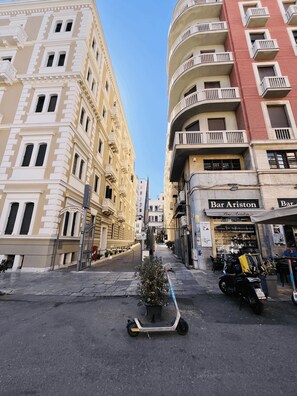 A street view with a narrow road flanked by multi-story buildings, including a hotel and a bar. - Politeama House 148 (Palermo)