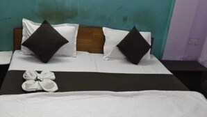 A hotel room with a bed, two pillows, a bedside table, and a wall-mounted light. - Hotel Rajshila (Prayagraj)