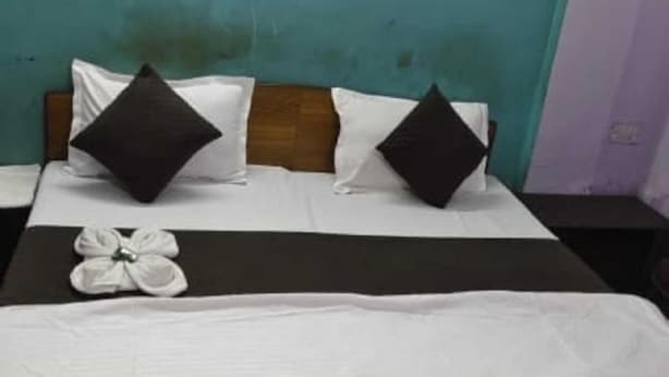 A hotel room with a bed, two pillows, a bedside table, and a wall-mounted light. - Hotel Rajshila (Prayagraj)
