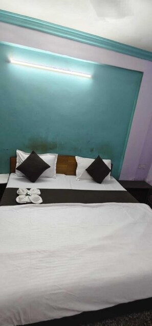A hotel room with a bed, two pillows, a bedside table, and a wall-mounted light. - Hotel Rajshila (Prayagraj)