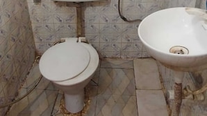 A bathroom with a toilet, a sink, and patterned tiles on the walls. - Hotel Rajshila (Prayagraj)
