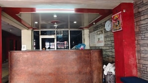 A reception area with a wooden counter, a clock on the wall, and a stone-textured wall to the right. - Hotel Rajshila (Prayagraj)