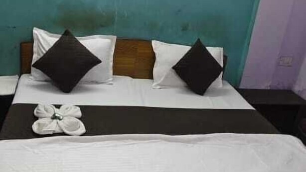 A neatly made bed with white and dark pillows, a black headboard, and a teal accent wall. - Hotel Rajshila (Prayagraj)