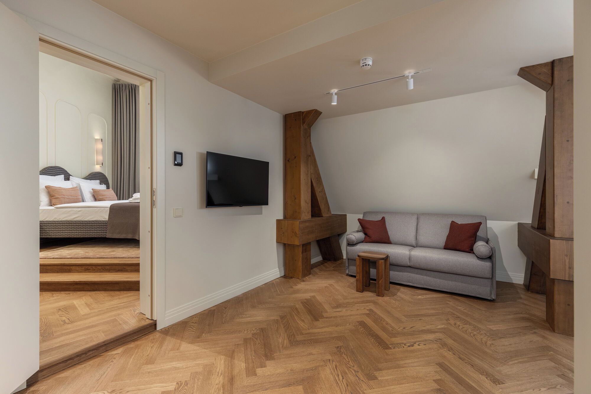 Une pièce moderne avec un plancher en bois, un canapé gris, une petite table en bois et un téléviseur à écran plat fixé au mur.