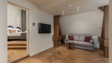 Una habitación moderna con piso de madera, un sofá gris, una pequeña mesa de madera y un televisor de pantalla plana montado en la pared.