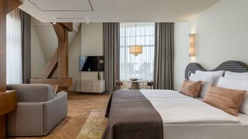 Una habitación de hotel moderna con una cama grande, un sofá, un televisor y una zona de comedor con una mesa y sillas.