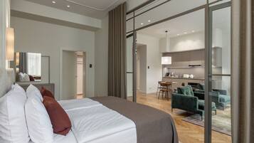 Habitación de hotel moderna con una cama grande, una zona de comedor separada y una cocina visible a través de una puerta de cristal.