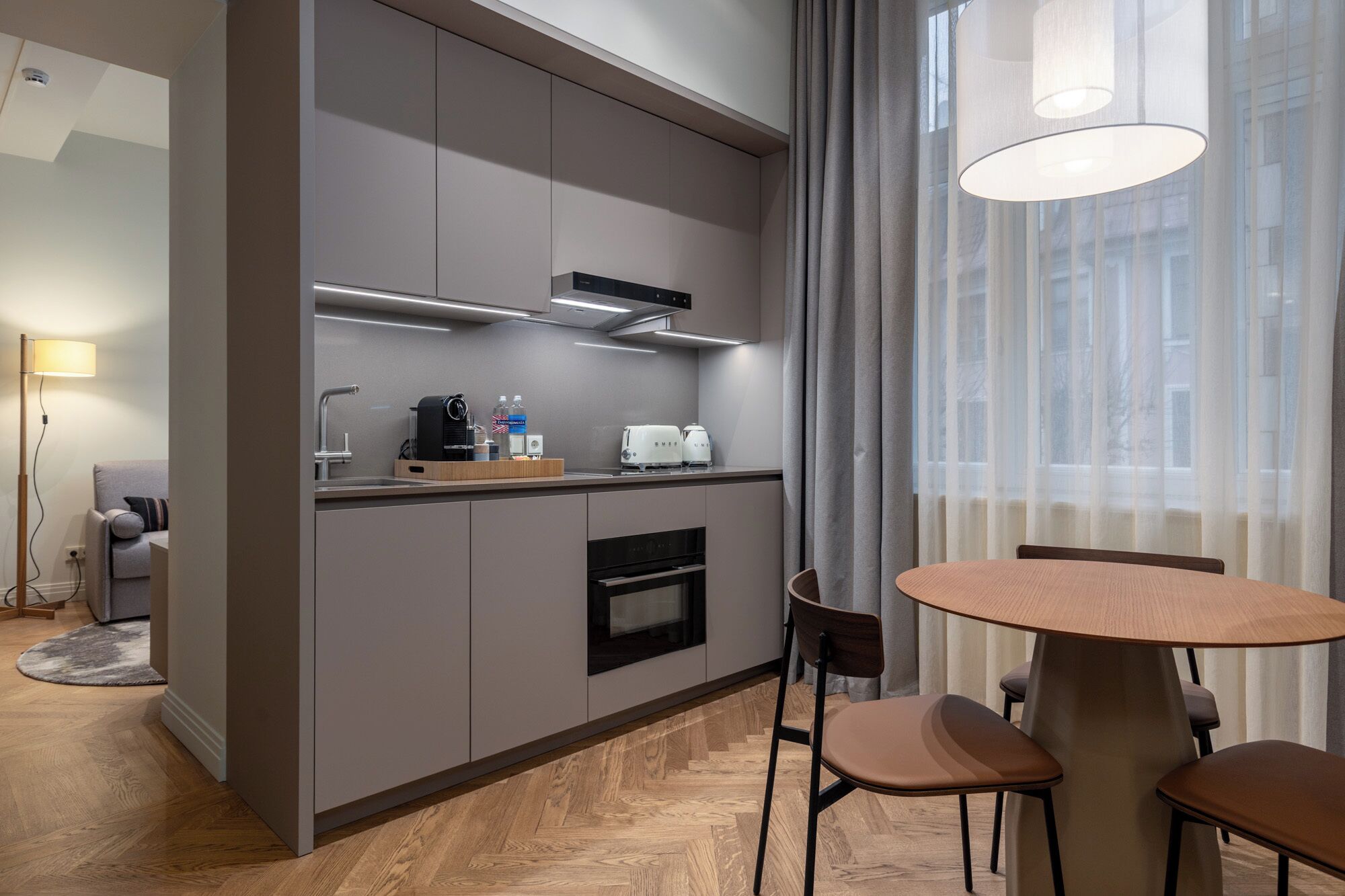 Una cocina moderna con armarios grises, horno empotrado y cafetera. Hay un comedor con una mesa redonda y cuatro sillas.