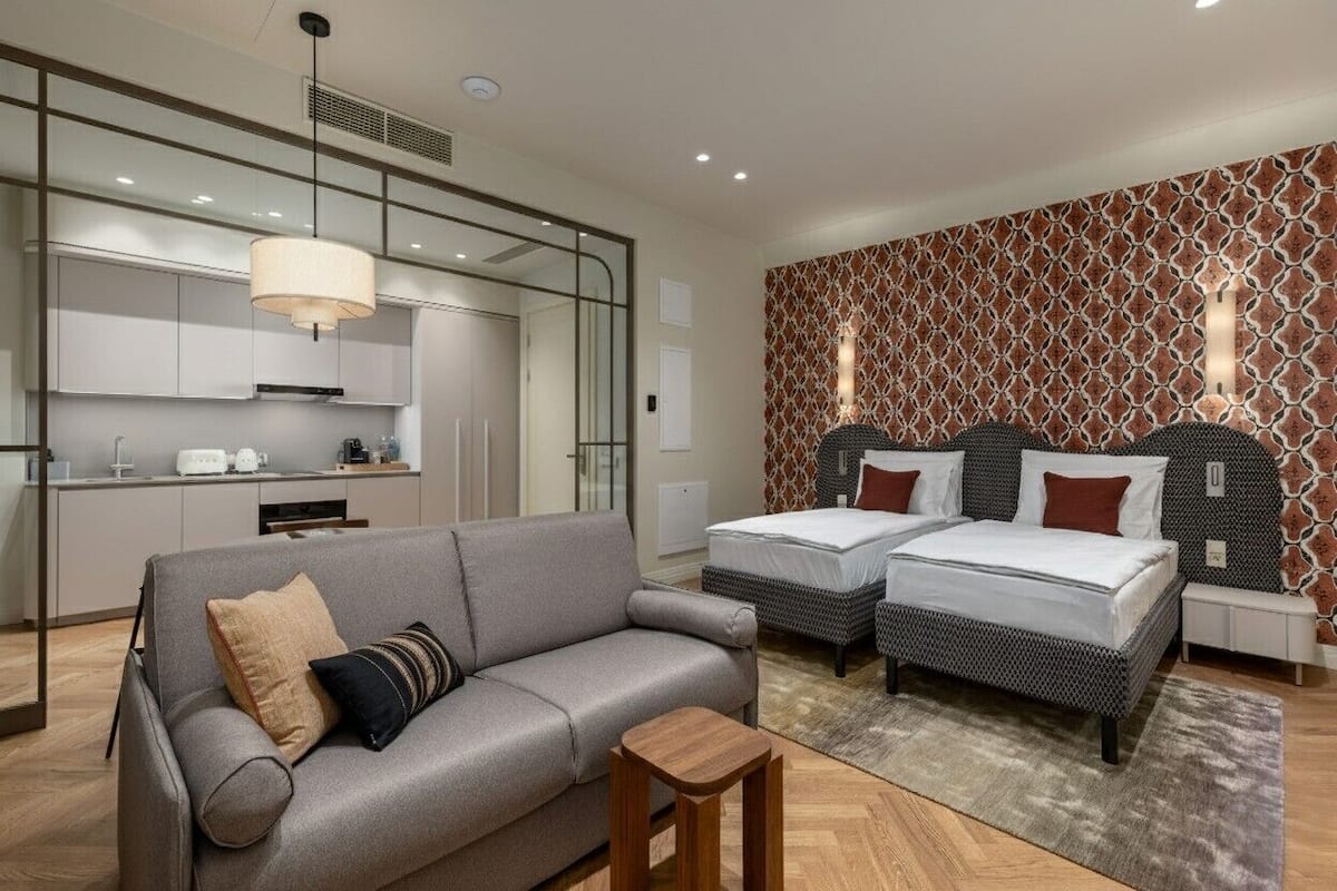 Une chambre d’hôtel moderne équipée d’un canapé, de deux lits, d’une petite table et d’un coin cuisine.