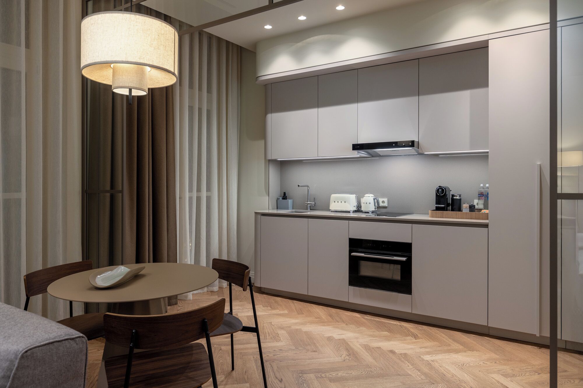 A modern kitchen with a round dining table, chairs, a built-in oven, and a coffee machine.