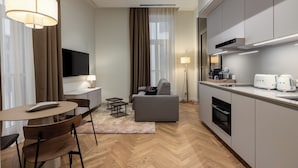 Habitación de hotel moderna con zona de comedor, sofá, televisión y kitchenette.