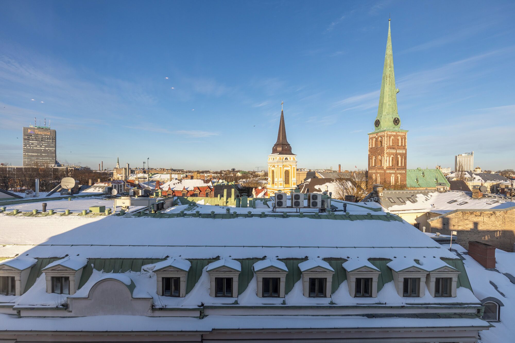 A snowy cityscape with a prominent church spire and a tall building in the background.
