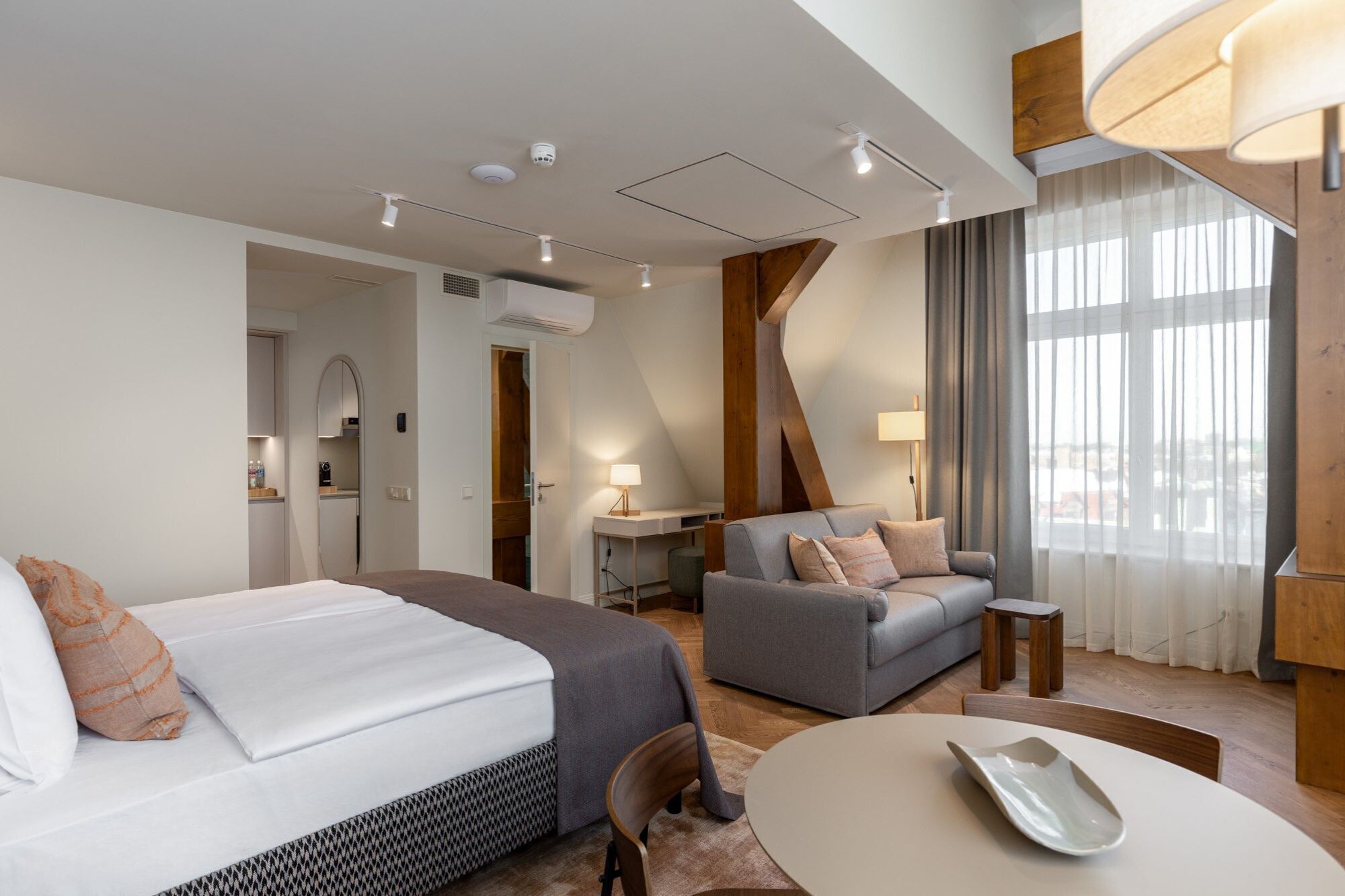 Una habitación de hotel moderna con cama, sofá, mesa y vistas a la ciudad a través de amplias ventanas.