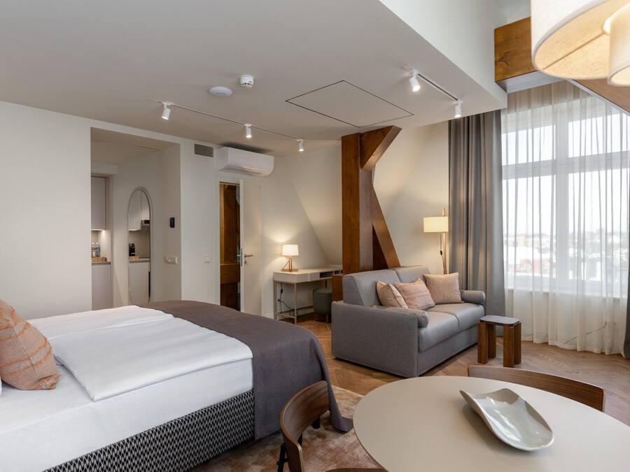 Una habitación de hotel moderna con cama, sofá, mesa y vistas a la ciudad a través de amplias ventanas.