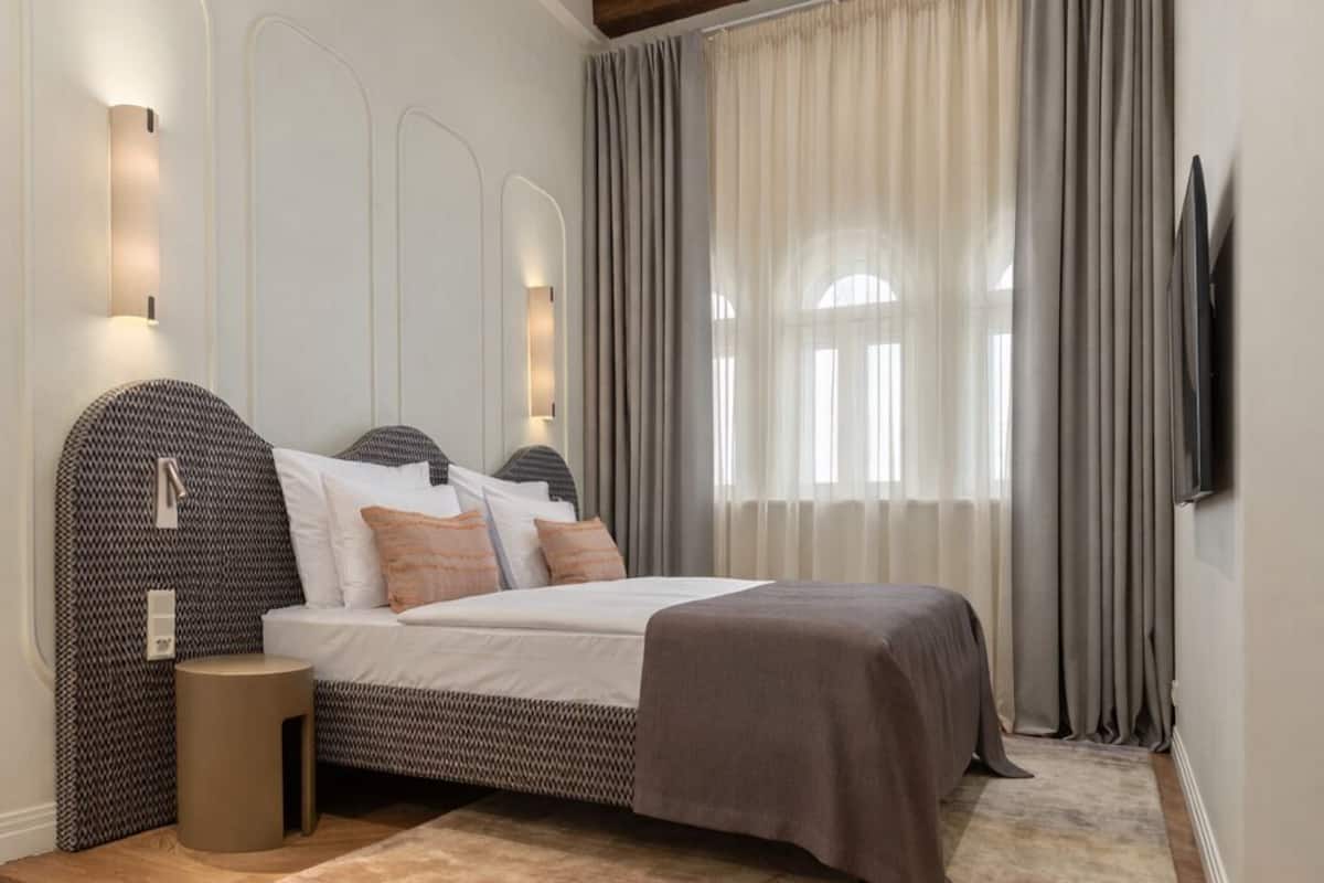 Une chambre à coucher avec un lit, des tables de chevet, une télévision et une fenêtre avec des rideaux.