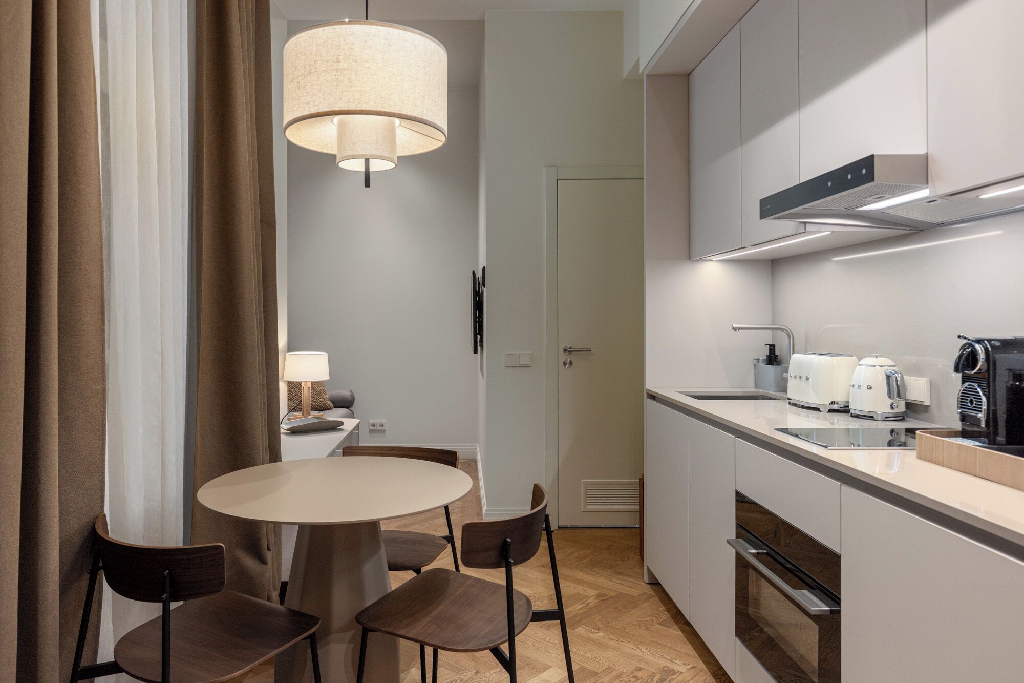 A modern kitchen with a round dining table, chairs, a hanging light fixture, and built-in appliances.