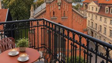 A balcony with a table and chairs, overlooking a historic building with a red brick facade and a church steeple.