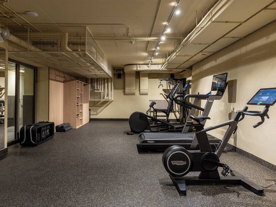 Un gimnasio con equipo de ejercicio, una escalera y un muro con espejos.