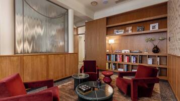 Un lobby moderno con una estantería de madera, sillas tapizadas en rojo, una mesa redonda y un cuadro abstracto grande.
