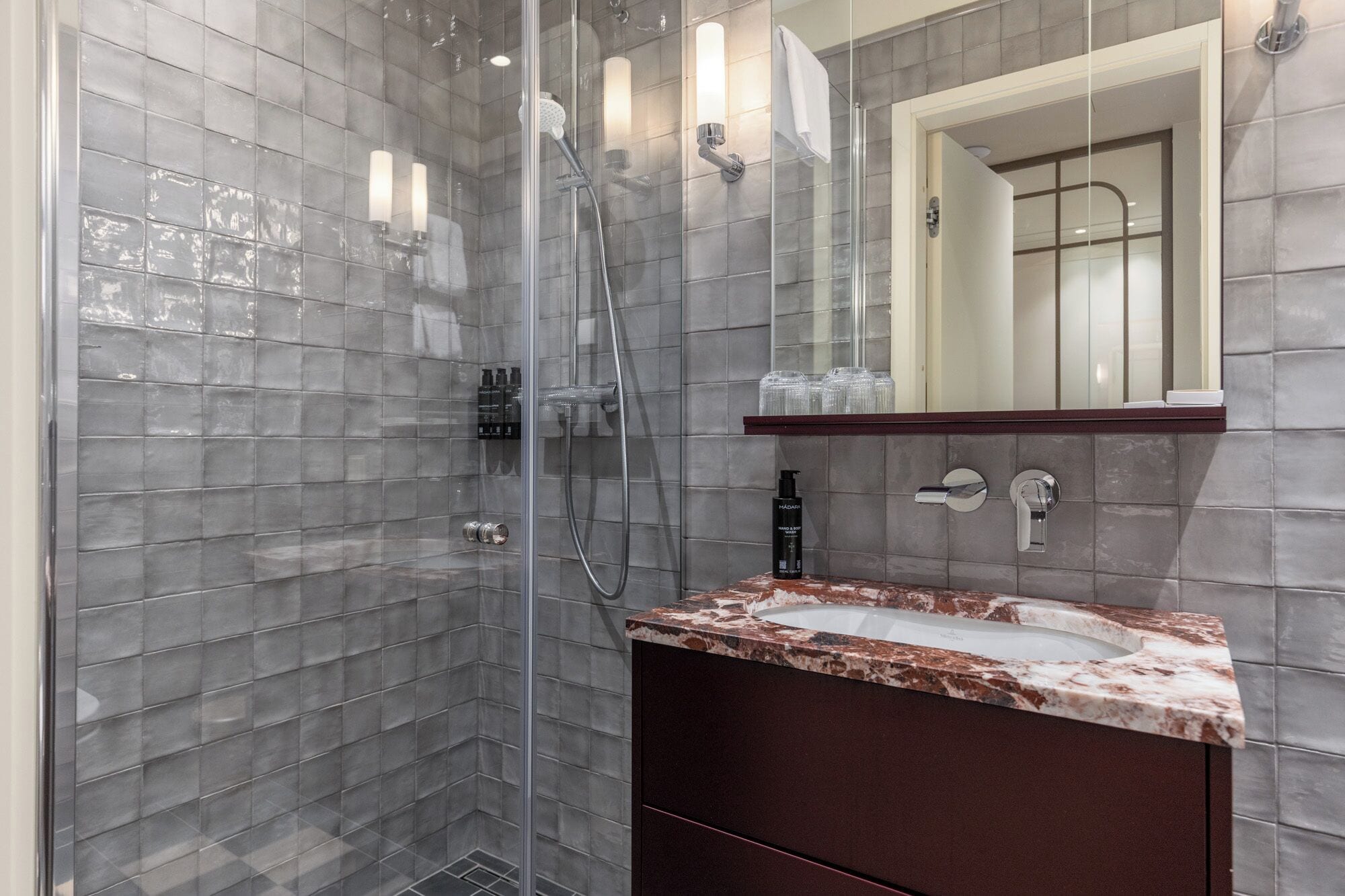 A modern bathroom with a glass-enclosed shower, a marble sink, and a large mirror.
