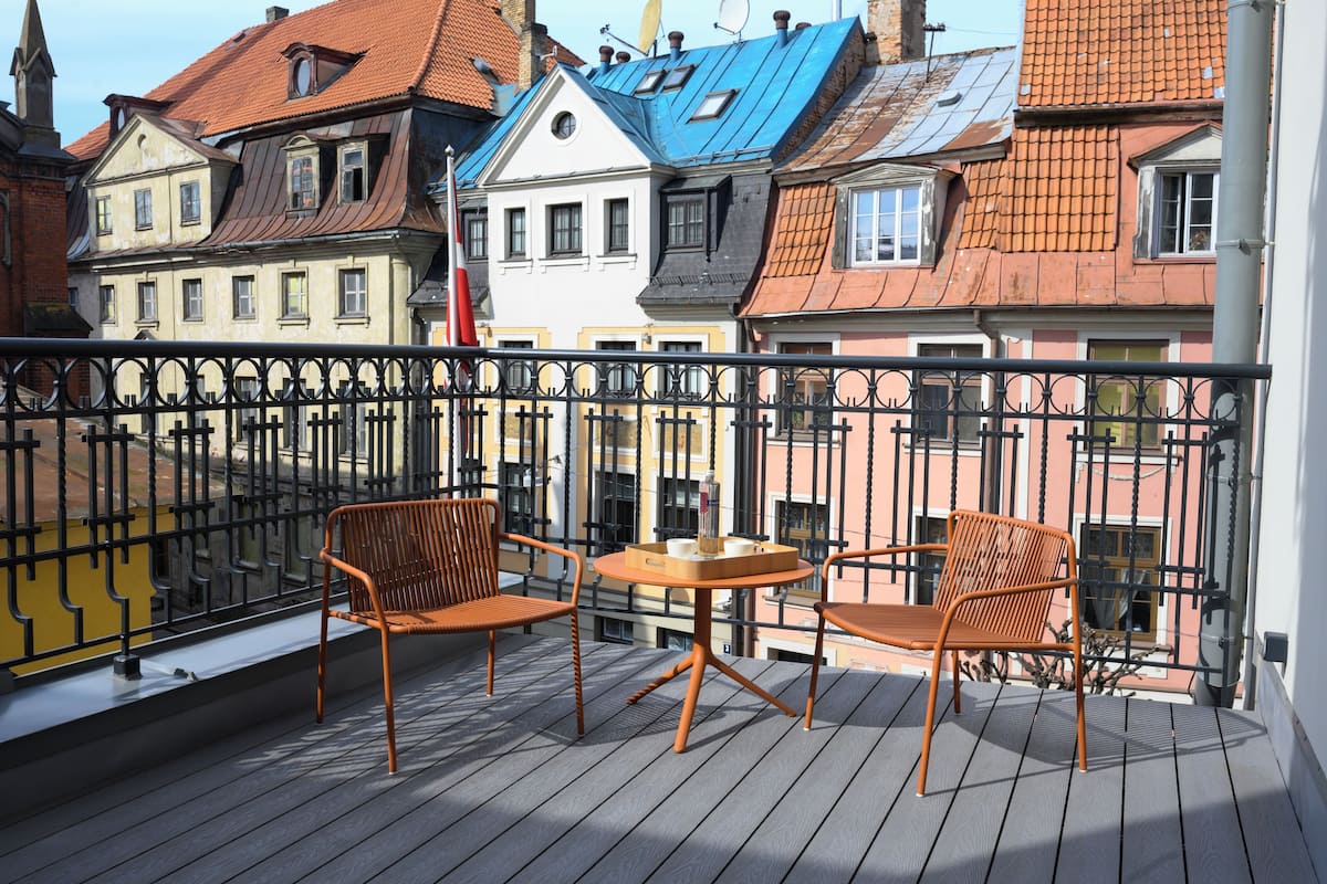 Un balcon avec deux chaises et une petite table, d’où l’on peut admirer des bâtiments aux couleurs vives et aux styles architecturaux bien distincts.