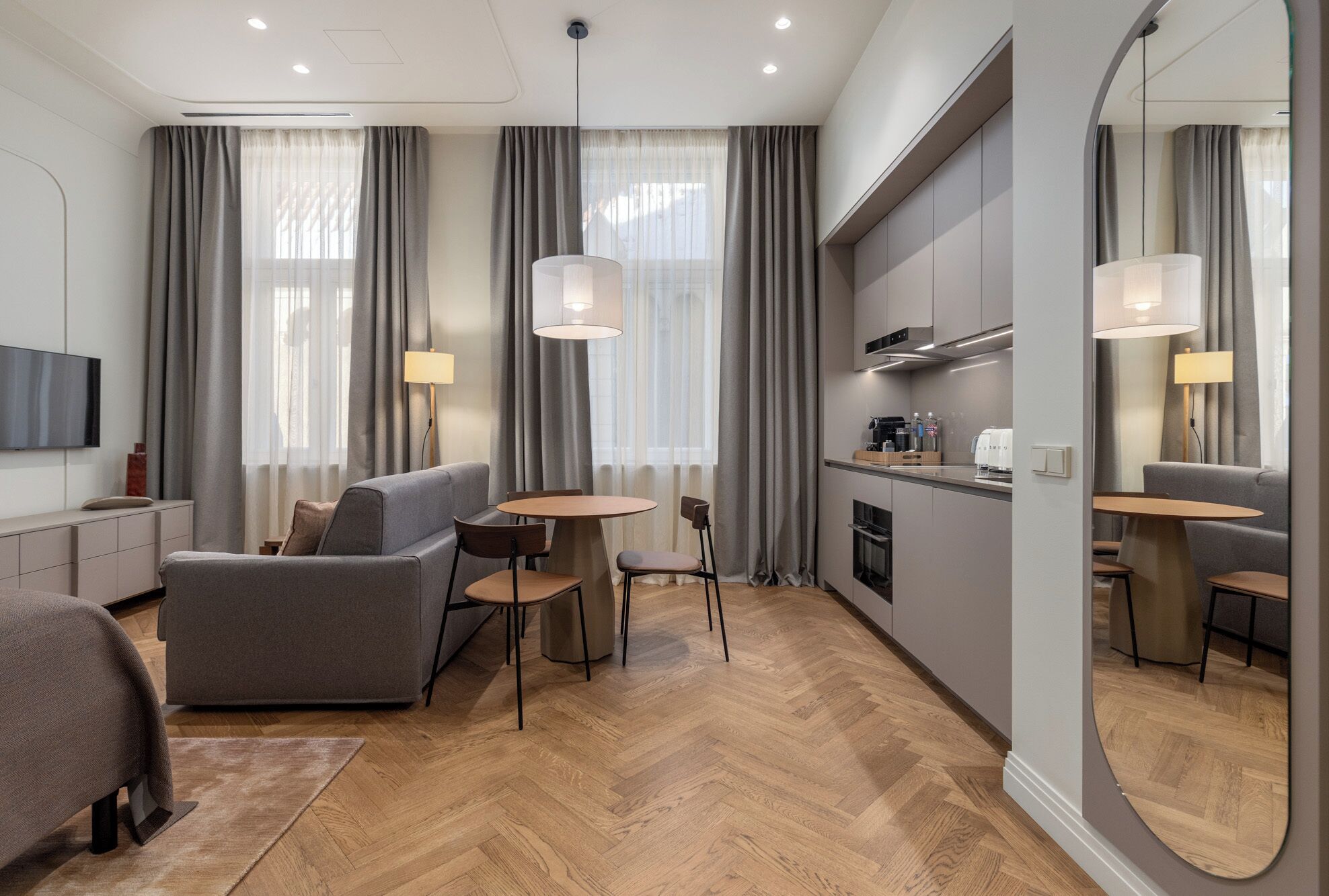 Moderni hotellihuone, jossa on sohva, pieni ruokapöytä, keittiöalue ja suuri peili.