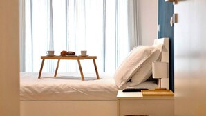 A neatly made bed with a bedside table, a lamp, and a small wooden table with a cup and pastries. - Santamaura86 Apartment (Roma)