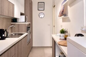 A modern kitchen with a built-in oven, a sink, and a clock on the wall.