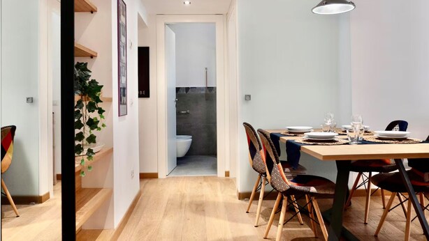 A modern dining area with a wooden table, chairs, and a hanging pendant light. A bathroom is visible through an open door in the background. - Santamaura86 Apartment (Roma)