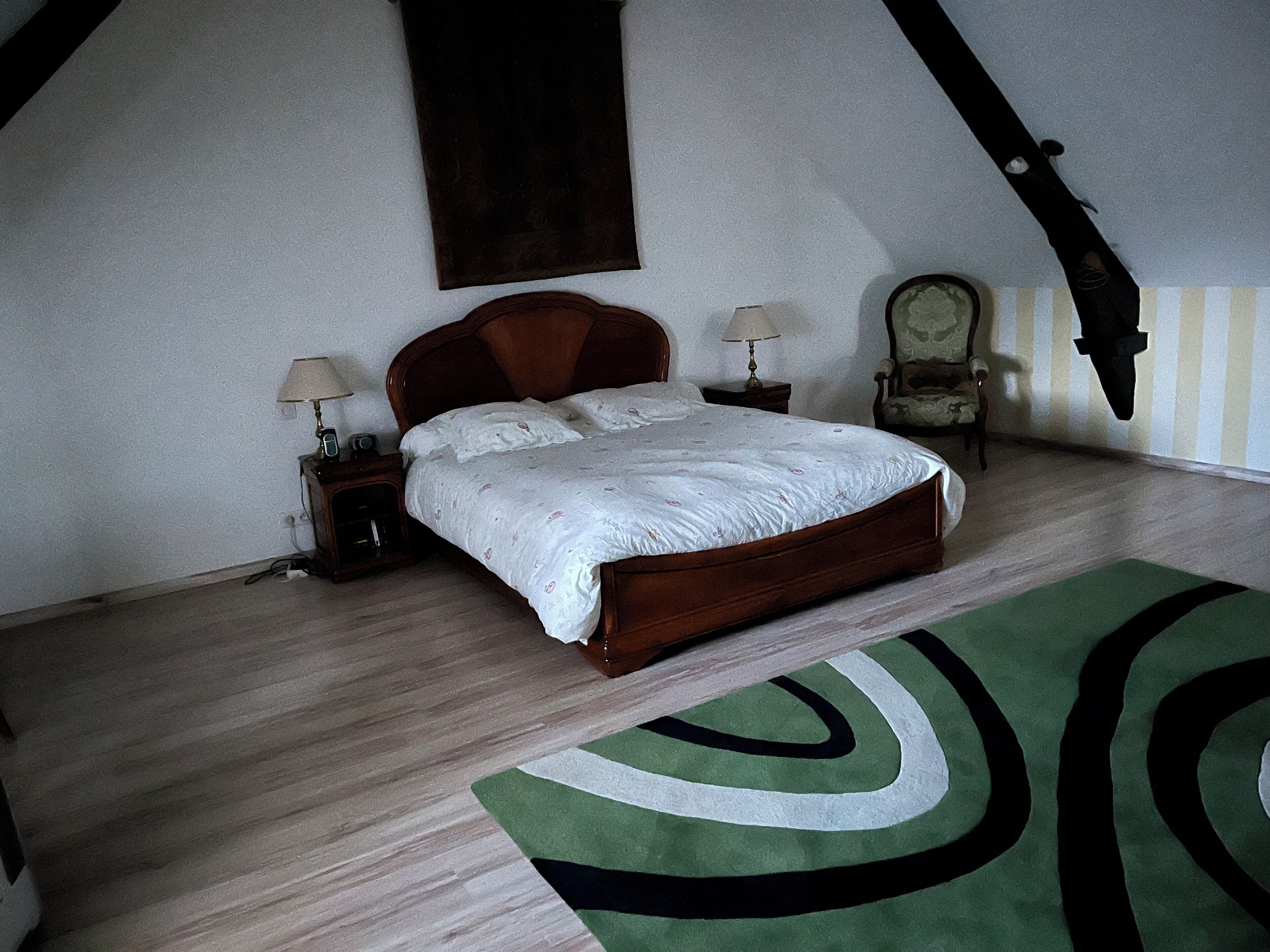 Un dormitorio con una cama de madera, dos mesitas de noche con lámparas, una silla y un tapete verde y blanco.