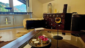 Un salón con una mesa de centro de cristal, un sofá de cuero negro, un aparador de madera con cajones y vistas al exterior a través de una ventana.