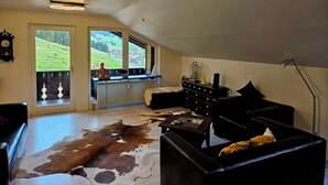 Amplia sala de estar con alfombra de cuero de vaca, muebles de cuero, vista a un paisaje verde a través de ventanas amplias y una lámpara de techo moderna.