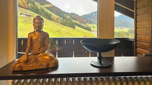 Una estatua de Buda sobre una mesa, con vistas a un paisaje montañoso a través de una ventana.