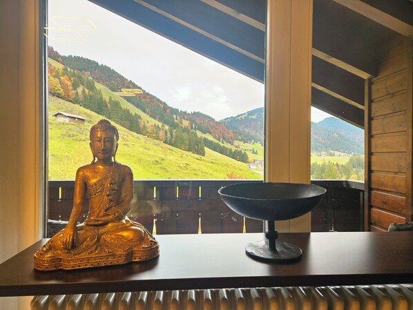 A Buddha statue on a table with a view of a mountainous landscape through a window.