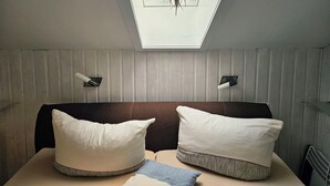 Una habitación con tragaluz, dos almohadas blancas, un plaid azul y un cabecero marrón.
