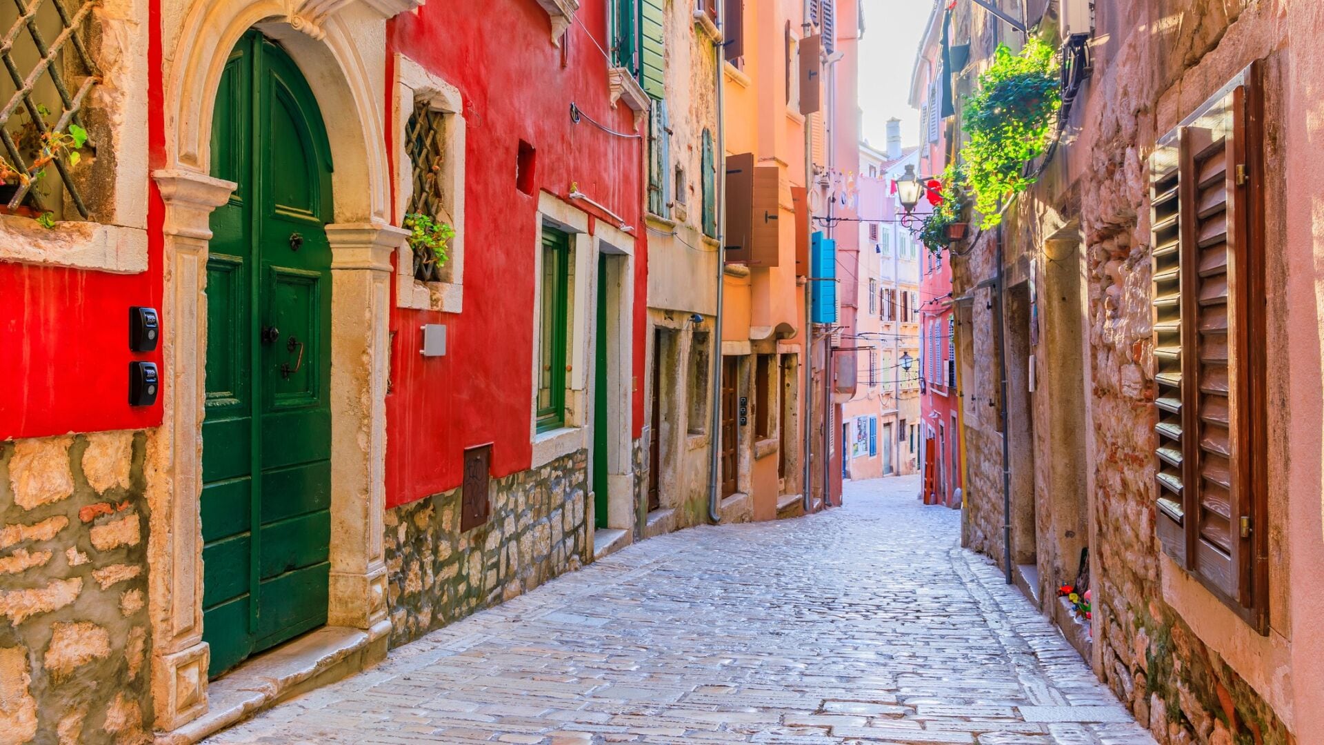 A narrow cobblestone street lined with colorful buildings, featuring stone walls and arched doorways.