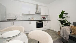 A modern kitchen with white cabinets, a microwave, and an oven. There is a dining table with chairs and a plant in the corner. - This is the One bright central 1BR well equiped. (Bedford)