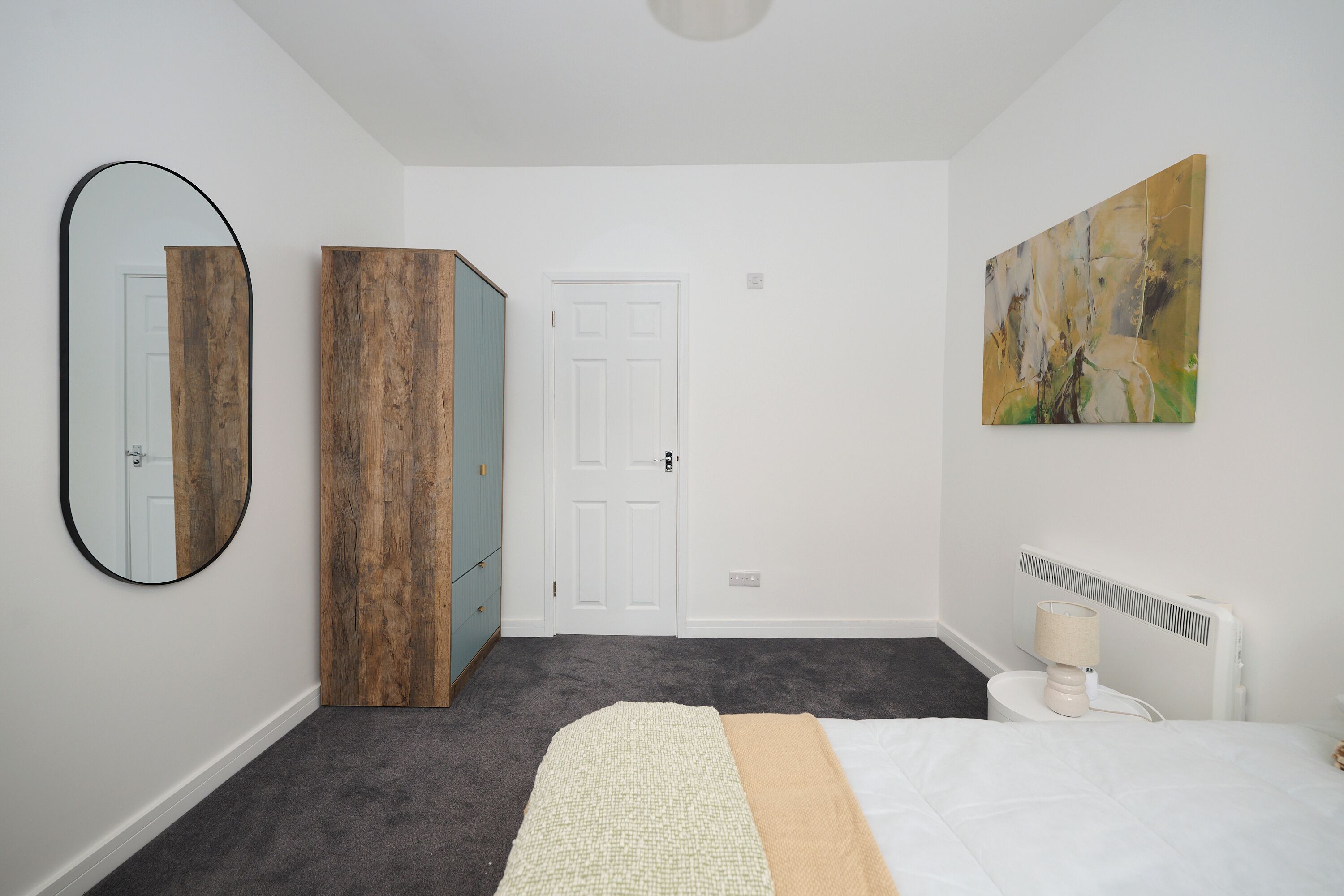 Een slaapkamer met een bed, een linnenkast, een spiegel en een schilderij aan de muur.