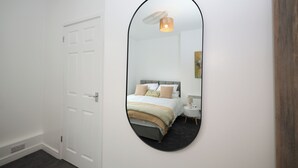 A bedroom with a white door, a round mirror, a bed with pillows, a bedside table, and a lamp. - This is the One bright central 1BR well equiped. (Bedford)