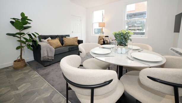 A modern dining area with a round table, white chairs, and a grey sofa. - This is the One bright central 1BR well equiped. (Bedford)