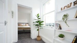 A hallway with a plant, a bookshelf with books and decorative items, and a bed in the adjacent room. - This is the One bright central 1BR well equiped. (Bedford)