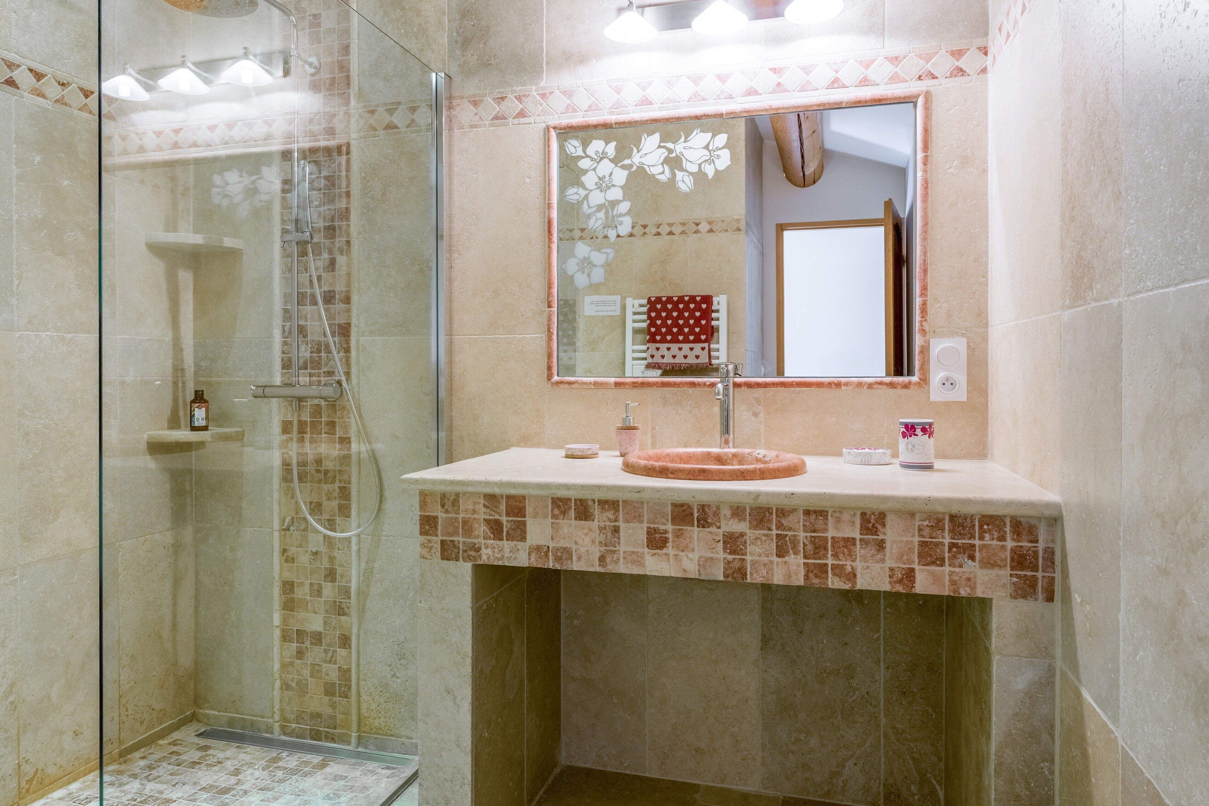 Une salle de bain avec une douche à parois de verre, un lavabo avec un miroir et un mur recouvert de carreaux.