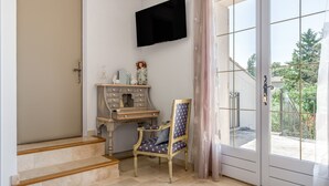A room with a desk, chair, TV, and a view through a glass door. - "Marcel Pagnol" Room at La Bastide des Mereuilles with Private Terrace, Wi-Fi & AC (Orange)