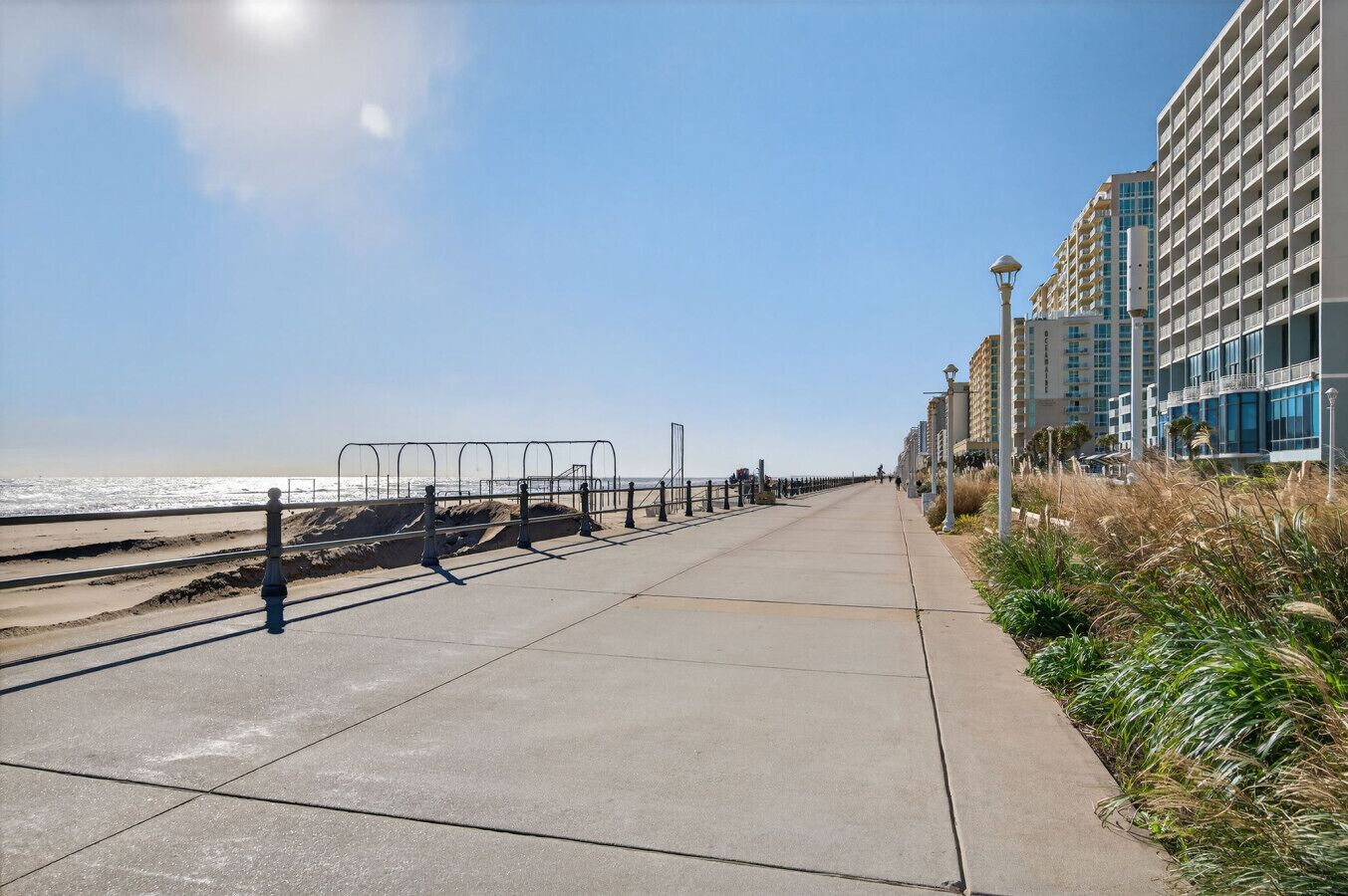 A coastal walkway with a beach on one side and a row of modern buildings.