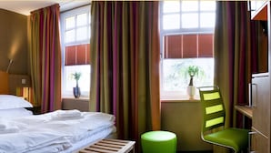 A hotel room with a bed, bedside tables, a chair, and a window with curtains.