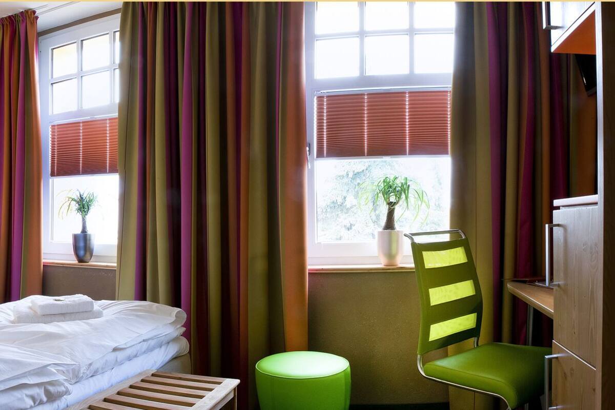 A hotel room with a bed, bedside tables, a chair, and a window with curtains.
