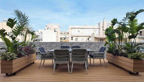 A wooden deck with a stone wall, wicker chairs, and planters with tropical plants.
