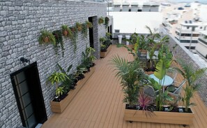 A rooftop terrace with stone walls, potted plants, and a seating area.