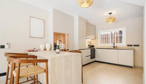 A modern kitchen with a central island, wooden chairs, and pendant lighting.