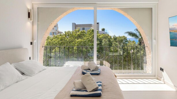 A bedroom with a large bed, a view through an arched window, and a balcony with a railing. - Casa Eva | Ref. #97 (Estepona)